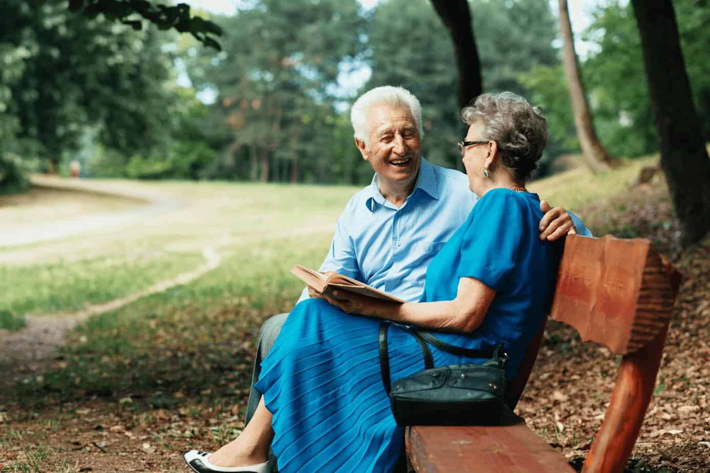 a senior couple sitting on a bench while holding their memory book