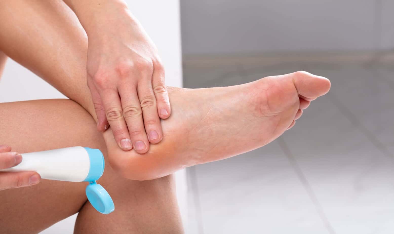 Close-up Of A Woman's Hand Applying Cream On Her Feet In House to help reduce aging on her feet