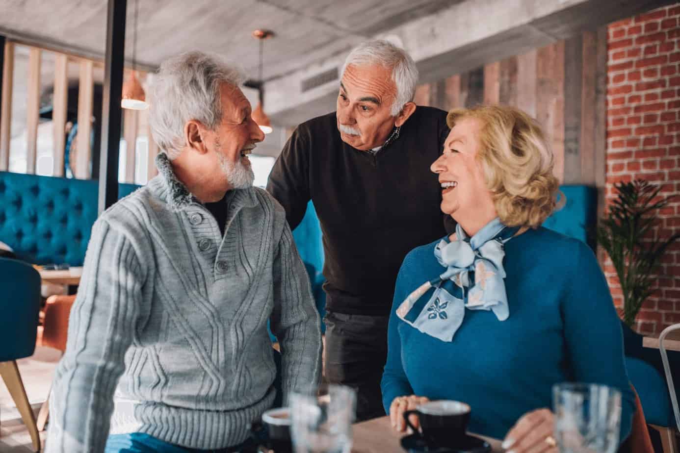 two old men talking to a beautiful old lady while drinking coffee