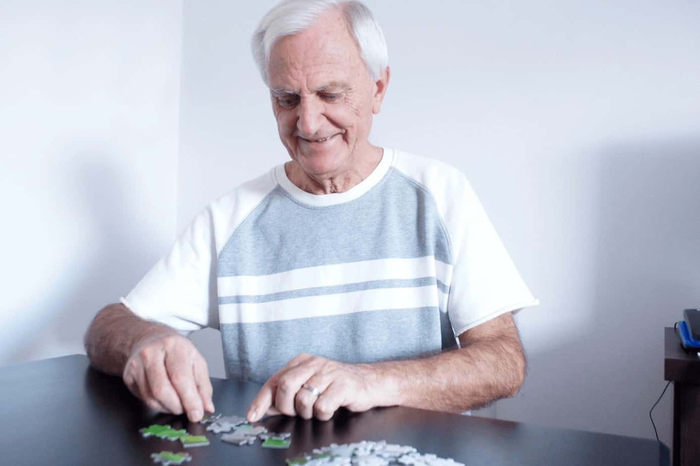 a senior man solving puzzle on a table, one of the easy activities for alzheimer's