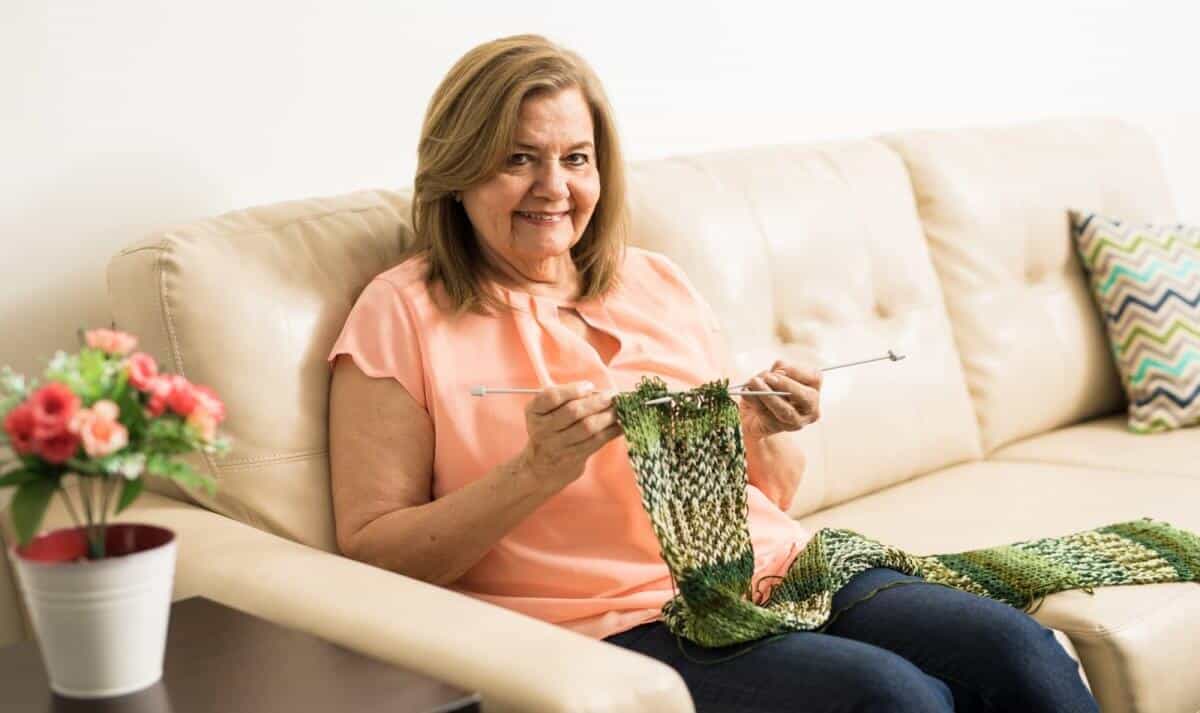 Happy senior woman working on her knitting skills and making a scarf, a very cute craft