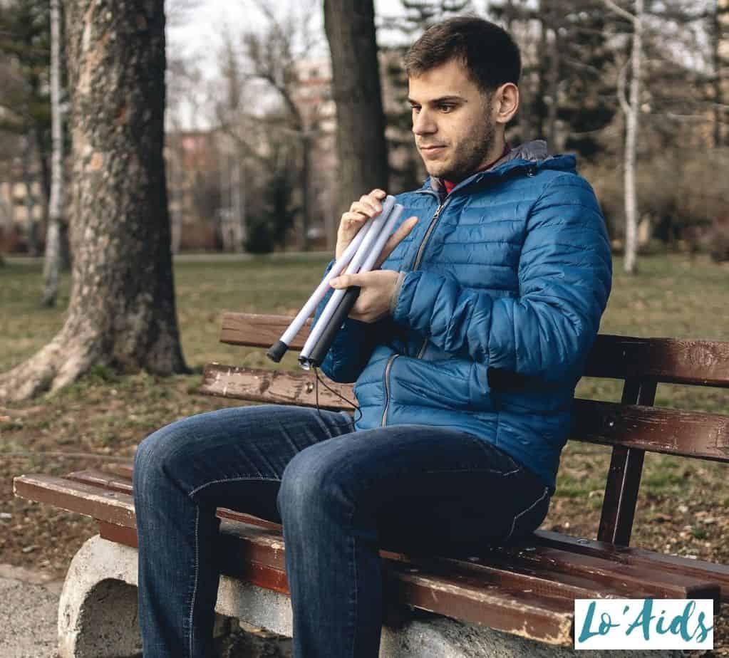 man holding a folding cane while sitting on a bench, one of the types of canes