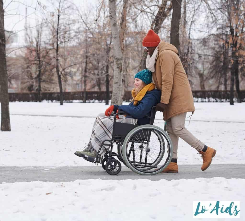 man pushing the wheelchair of his girlfriend in the snowy road