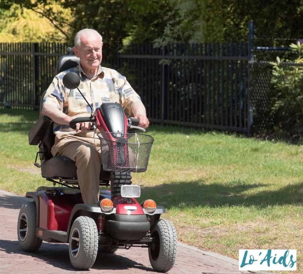 A smiling elderly man riding a red and black scooter