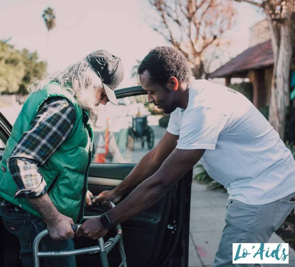 elderly man using a walker being helped by a young man